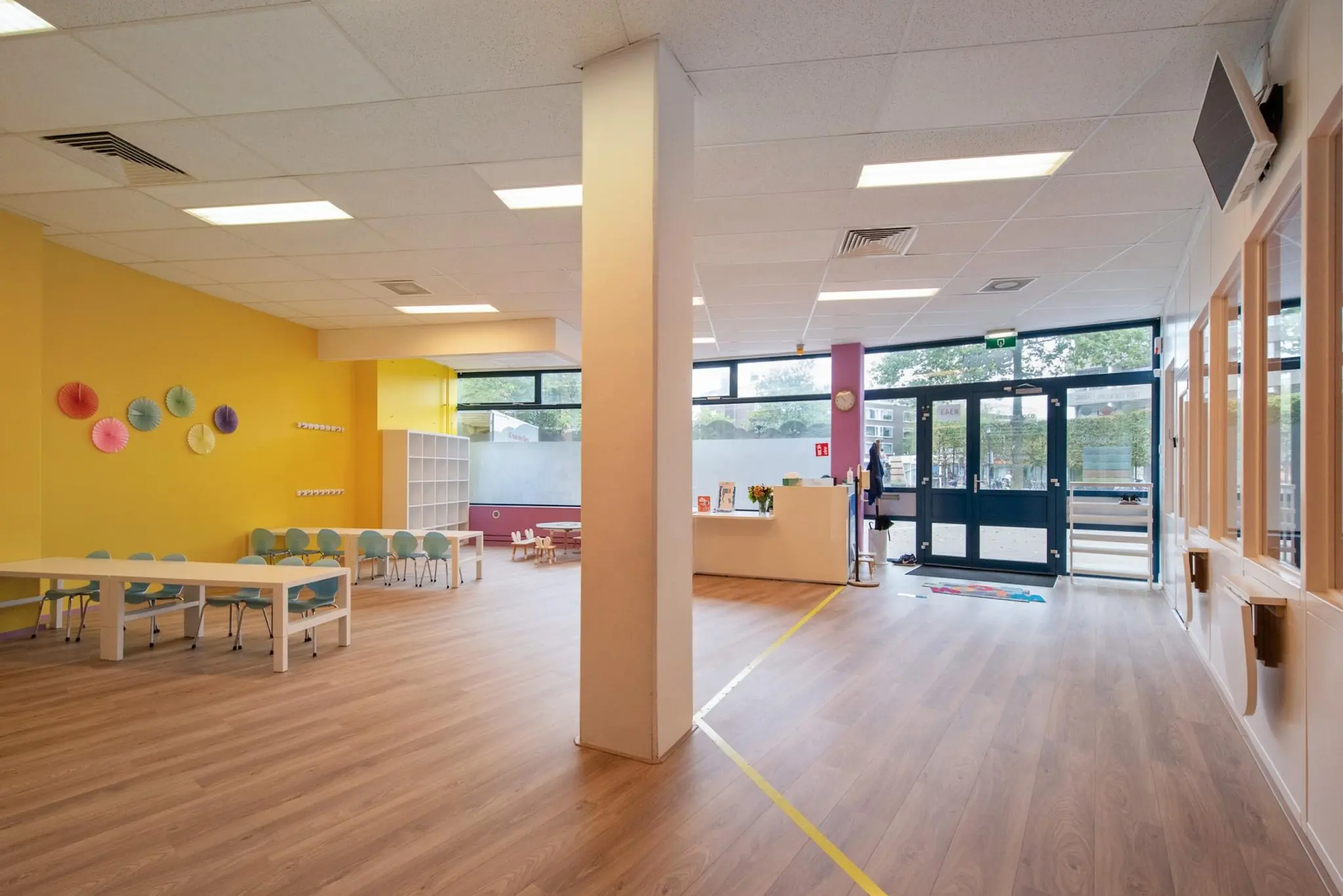 Licht en ruim klaslokaal van een basisschool aan de Koningin Julianalaan met kleurrijke stoelen, tafels en decoraties.